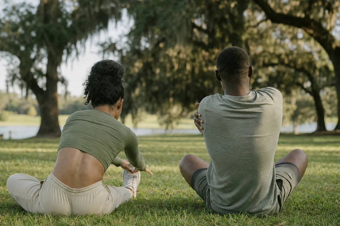 Two people seen from behind, sitting on the grass and stretching after a workout